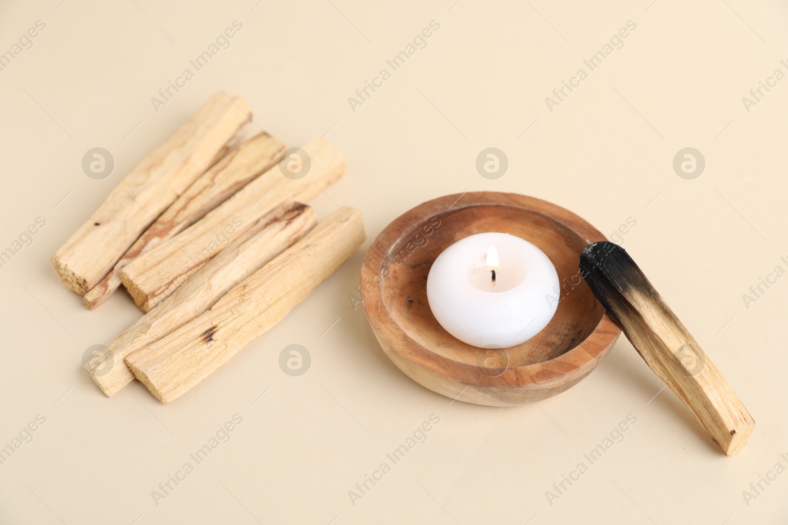 Photo of Palo santo sticks, burnt one and burning candle on beige background, closeup