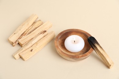 Photo of Palo santo sticks, burnt one and burning candle on beige background, closeup