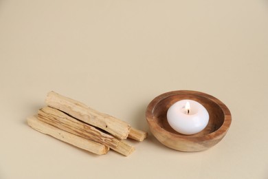 Photo of Palo santo sticks and burning candle on beige background, closeup