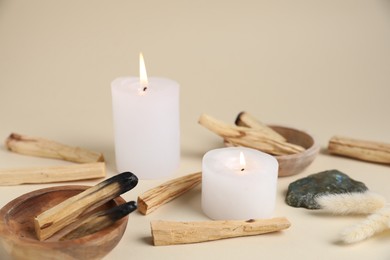 Photo of Palo santo sticks, burning candles, gemstone and dry spikes on beige background, closeup