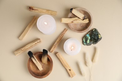 Photo of Palo santo sticks, burning candles, gemstone and dry spikes on beige background, flat lay