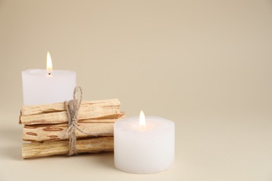 Photo of Bunch of palo santo sticks and burning candles on beige background, closeup. Space for text