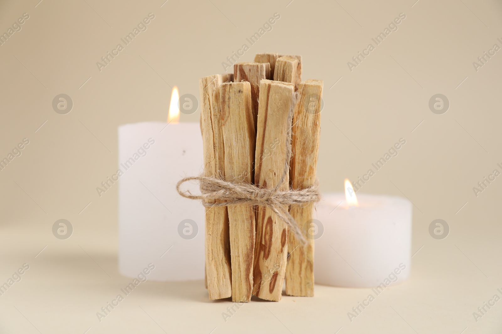 Photo of Bunch of palo santo sticks and burning candles on beige background