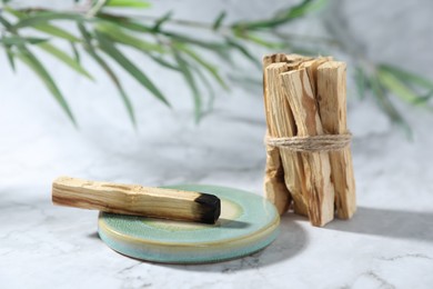 Photo of Palo santo sticks, burnt one and green branch on white marble table, closeup