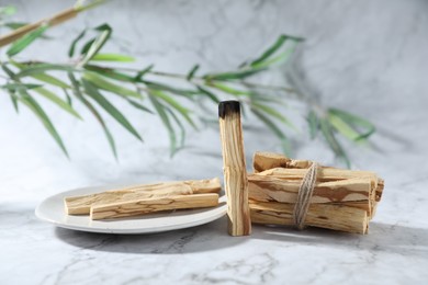 Photo of Palo santo sticks, burnt one and green branch on white marble table, closeup