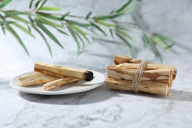 Photo of Palo santo sticks, burnt one and green branch on white marble table, closeup