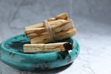 Photo of Palo santo sticks and smoldering one on white marble table, closeup. Space for text