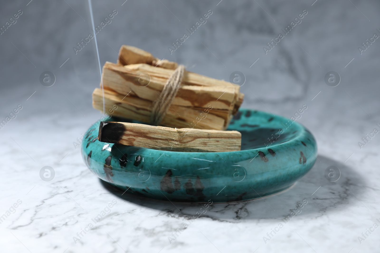 Photo of Palo santo sticks and smoldering one on white marble table, closeup