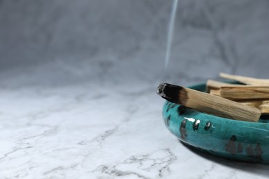 Photo of Smoldering palo santo stick on white marble table, closeup. Space for text