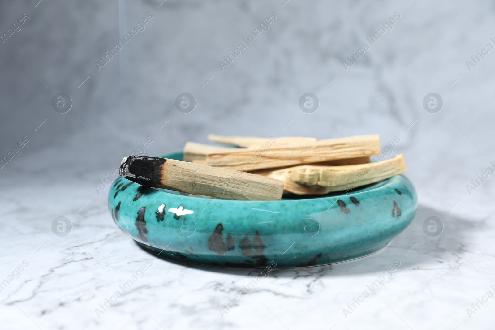 Photo of Palo santo sticks and smoldering one on white marble table, closeup