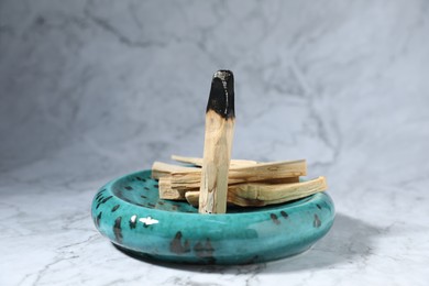 Photo of Palo santo sticks and burnt one on white marble table, closeup