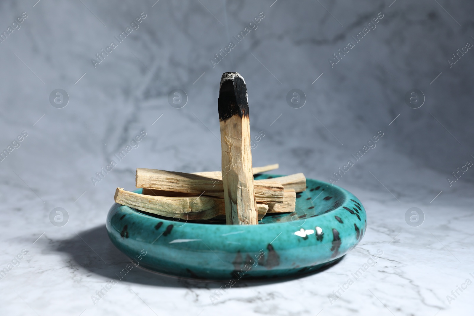 Photo of Palo santo sticks and smoldering one on white marble table, closeup