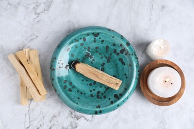 Photo of Palo santo sticks, burnt one and burning candles on white marble table, flat lay