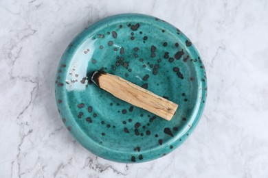 Photo of Burnt palo santo stick on white marble table, top view