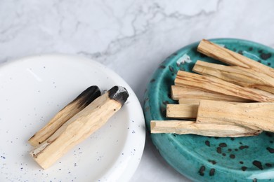 Photo of Whole and burnt palo santo sticks on white marble table, closeup