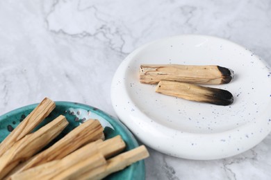 Photo of Whole and burnt palo santo sticks on white marble table, closeup