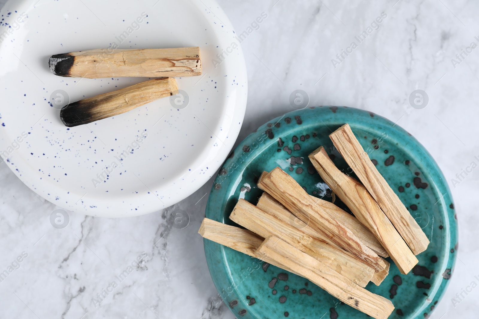 Photo of Whole and burnt palo santo sticks on white marble table, flat lay