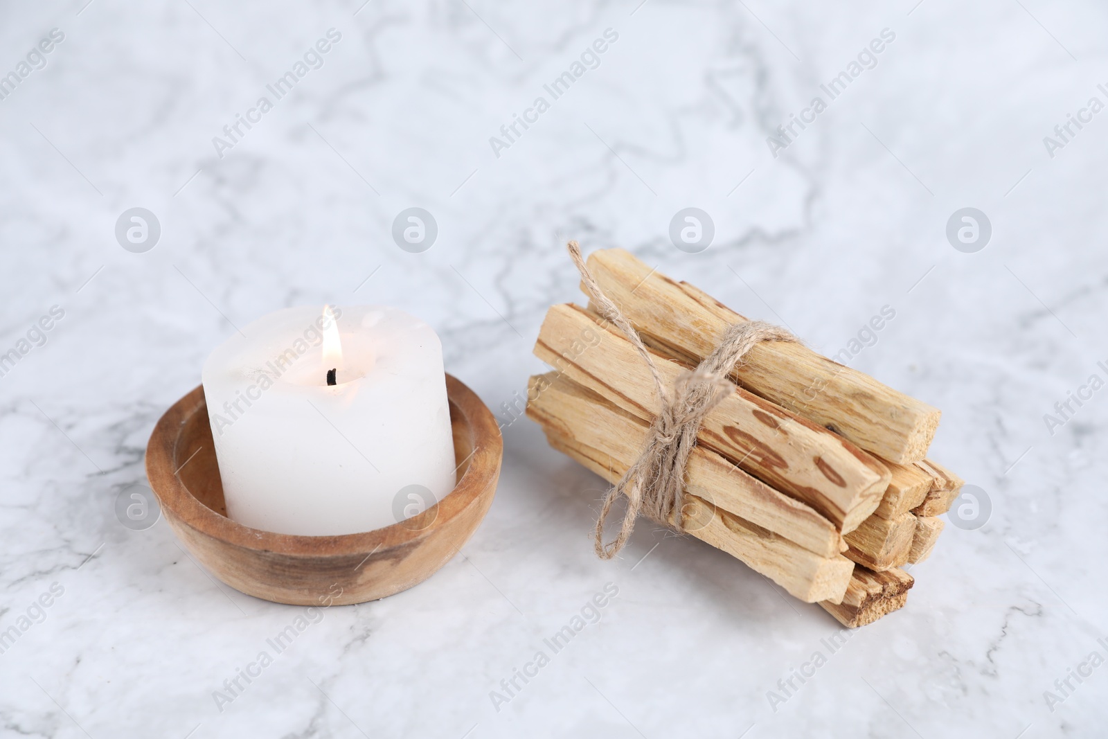 Photo of Bunch of palo santo sticks and burning candle on white marble table, closeup