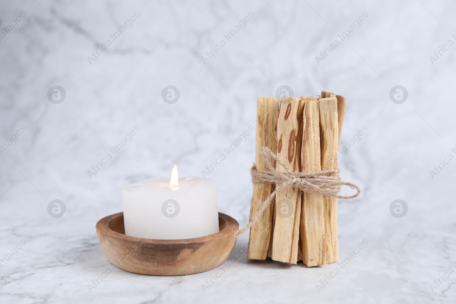 Photo of Bunch of palo santo sticks and burning candle on white marble table