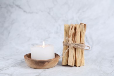 Photo of Bunch of palo santo sticks and burning candle on white marble table