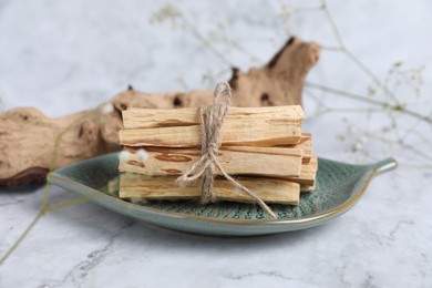 Photo of Bunch of palo santo sticks, snag and gypsophila flowers on white marble table, closeup