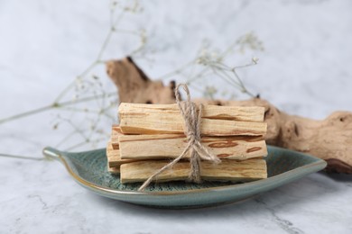 Photo of Bunch of palo santo sticks, snag and gypsophila flowers on white marble table, closeup