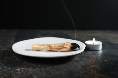 Photo of Smoldering palo santo stick and burning candle on dark table, closeup