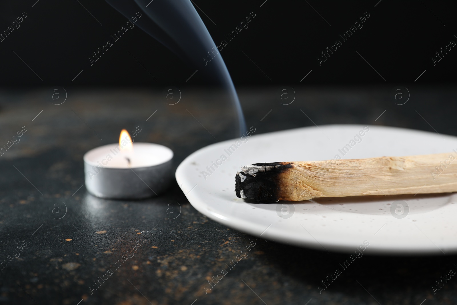 Photo of Smoldering palo santo stick and burning candle on dark table, closeup