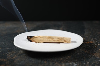 Photo of Smoldering palo santo stick on dark table, closeup