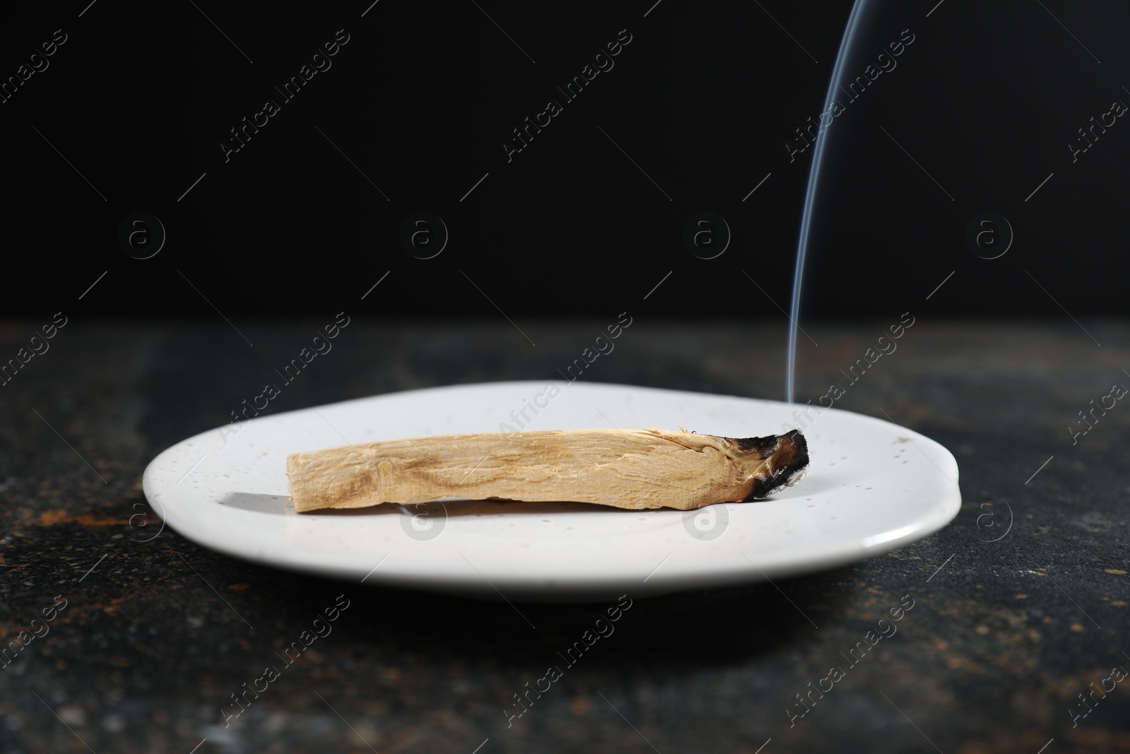 Photo of Smoldering palo santo stick on dark table, closeup