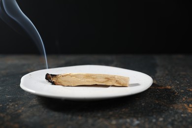 Photo of Smoldering palo santo stick on dark table, closeup