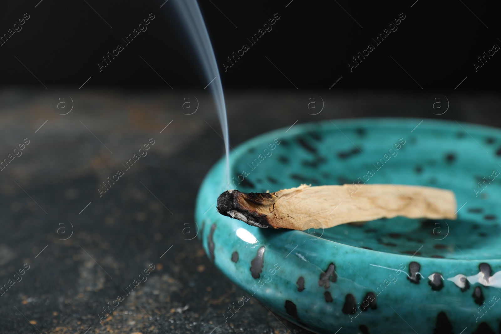 Photo of Smoldering palo santo stick on dark table, closeup. Space for text