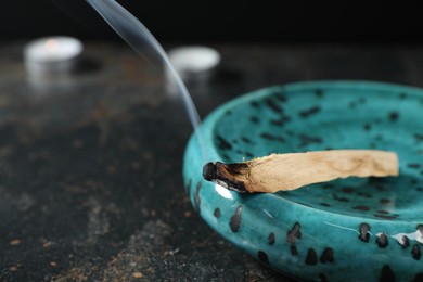 Photo of Smoldering palo santo stick on dark table, closeup. Space for text