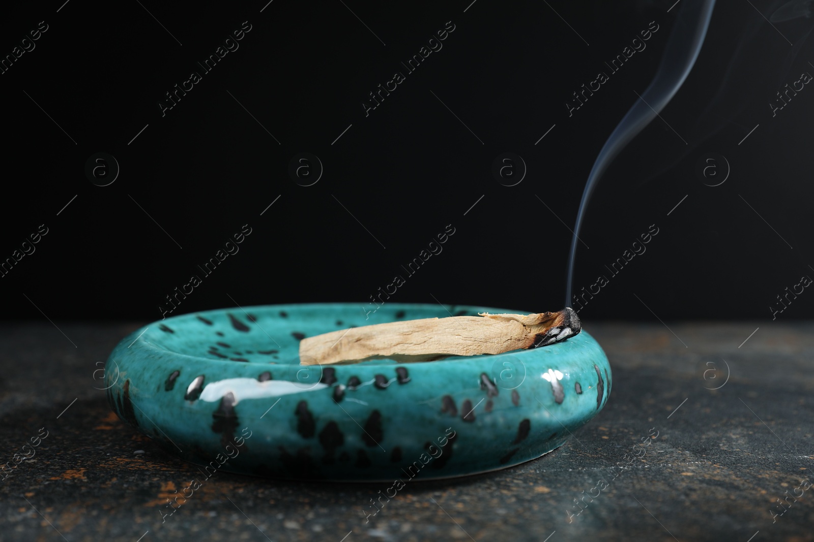 Photo of Smoldering palo santo stick on dark table, closeup