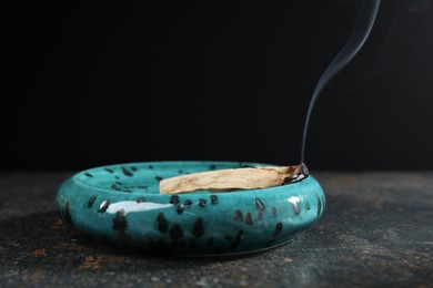 Photo of Smoldering palo santo stick on dark table, closeup