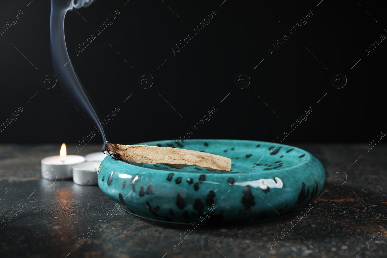 Photo of Smoldering palo santo stick and burning candles on dark table, closeup