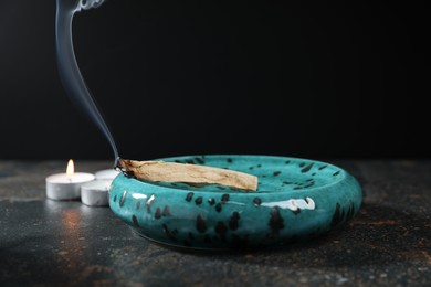 Photo of Smoldering palo santo stick and burning candles on dark table, closeup