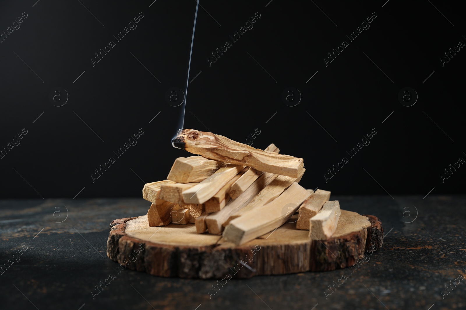 Photo of Palo santo sticks and smoldering one on dark table