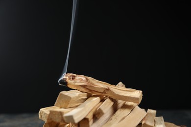 Photo of Palo santo sticks and smoldering one on black background, closeup