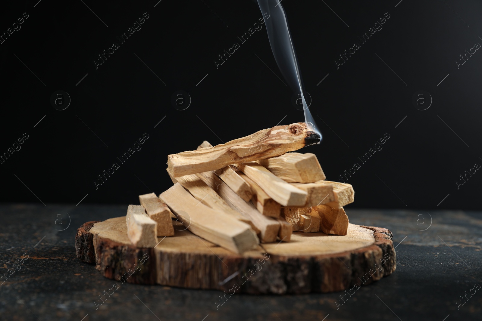 Photo of Palo santo sticks and smoldering one on dark table, closeup