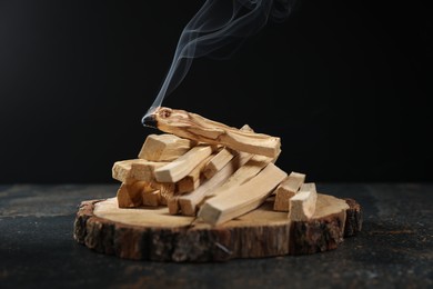 Photo of Palo santo sticks and smoldering one on dark table, closeup