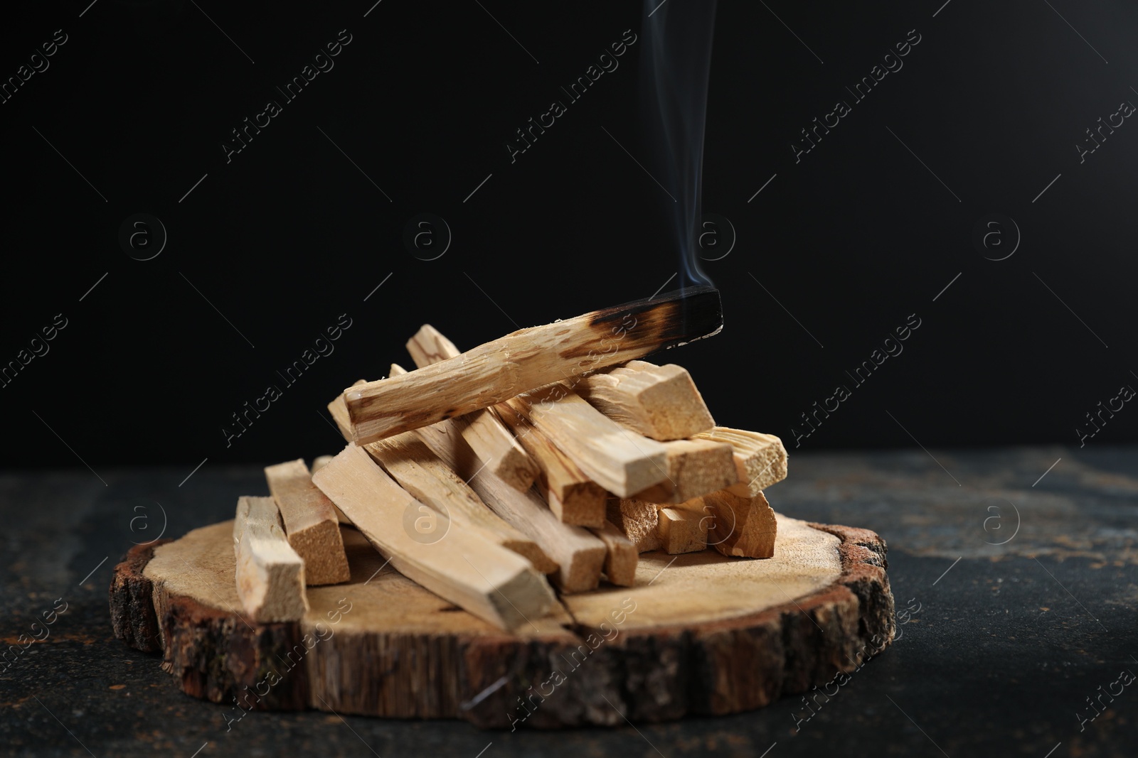 Photo of Palo santo sticks and smoldering one on dark table, closeup