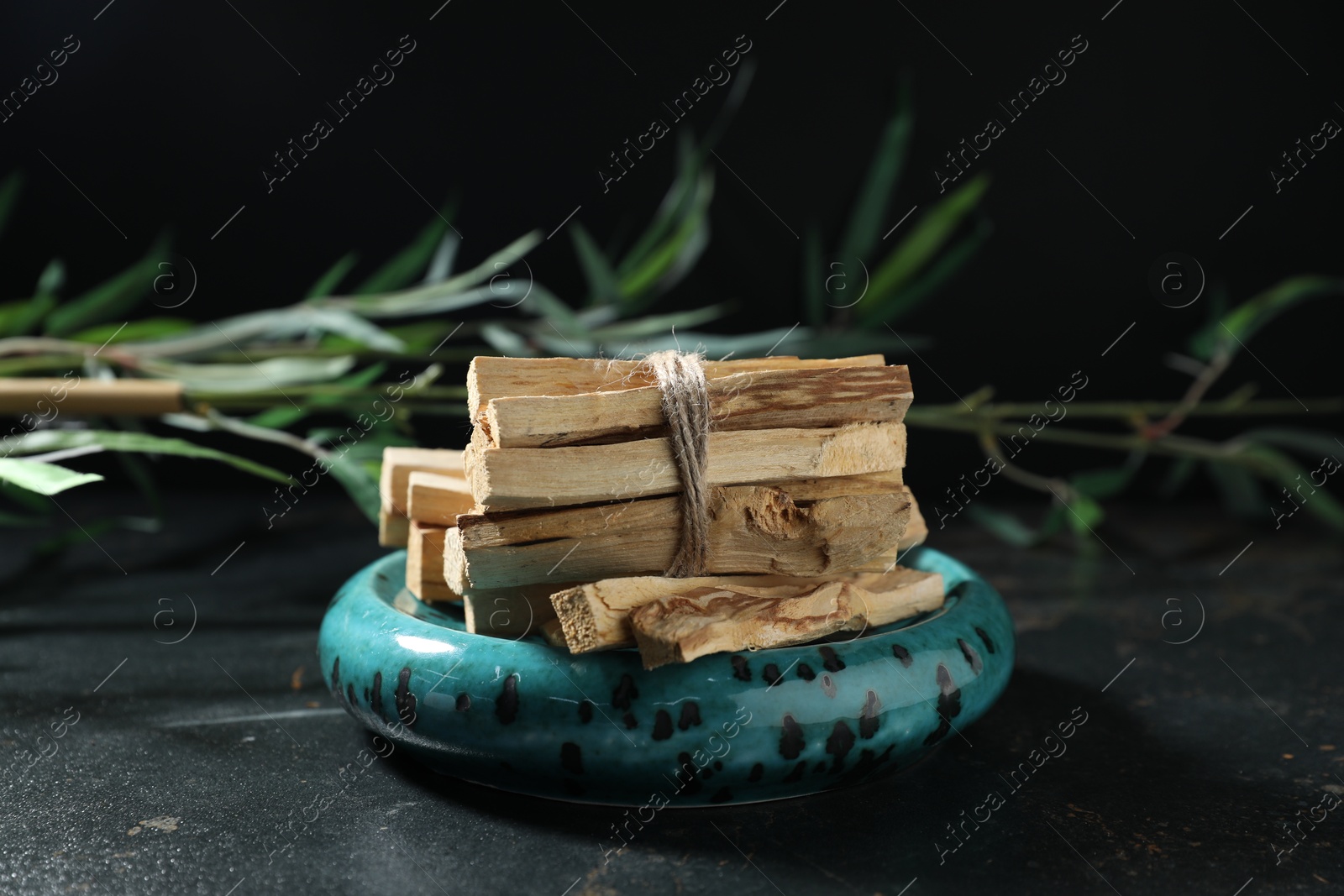 Photo of Bunch of palo santo sticks and green branch on dark table, closeup