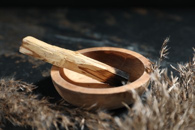 Photo of Burnt palo santo stick and dried reed on dark table, closeup