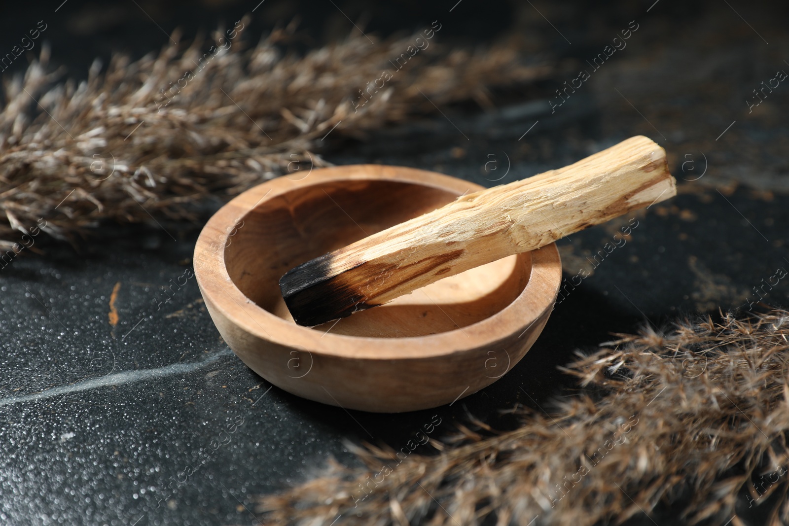 Photo of Burnt palo santo stick and dried reed on dark table, closeup