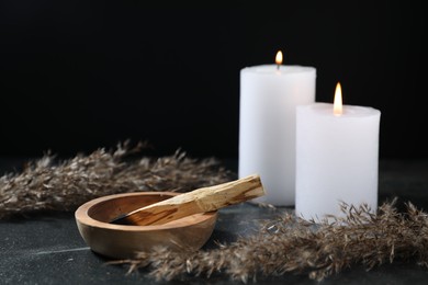 Photo of Burnt palo santo stick, burning candles and dried reed on dark table, closeup