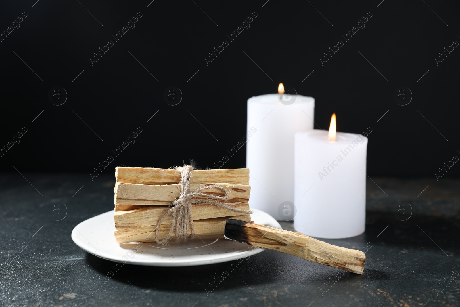 Photo of Palo santo sticks, burnt one and burning candles on dark table, closeup