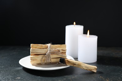 Photo of Palo santo sticks, burnt one and burning candles on dark table, closeup