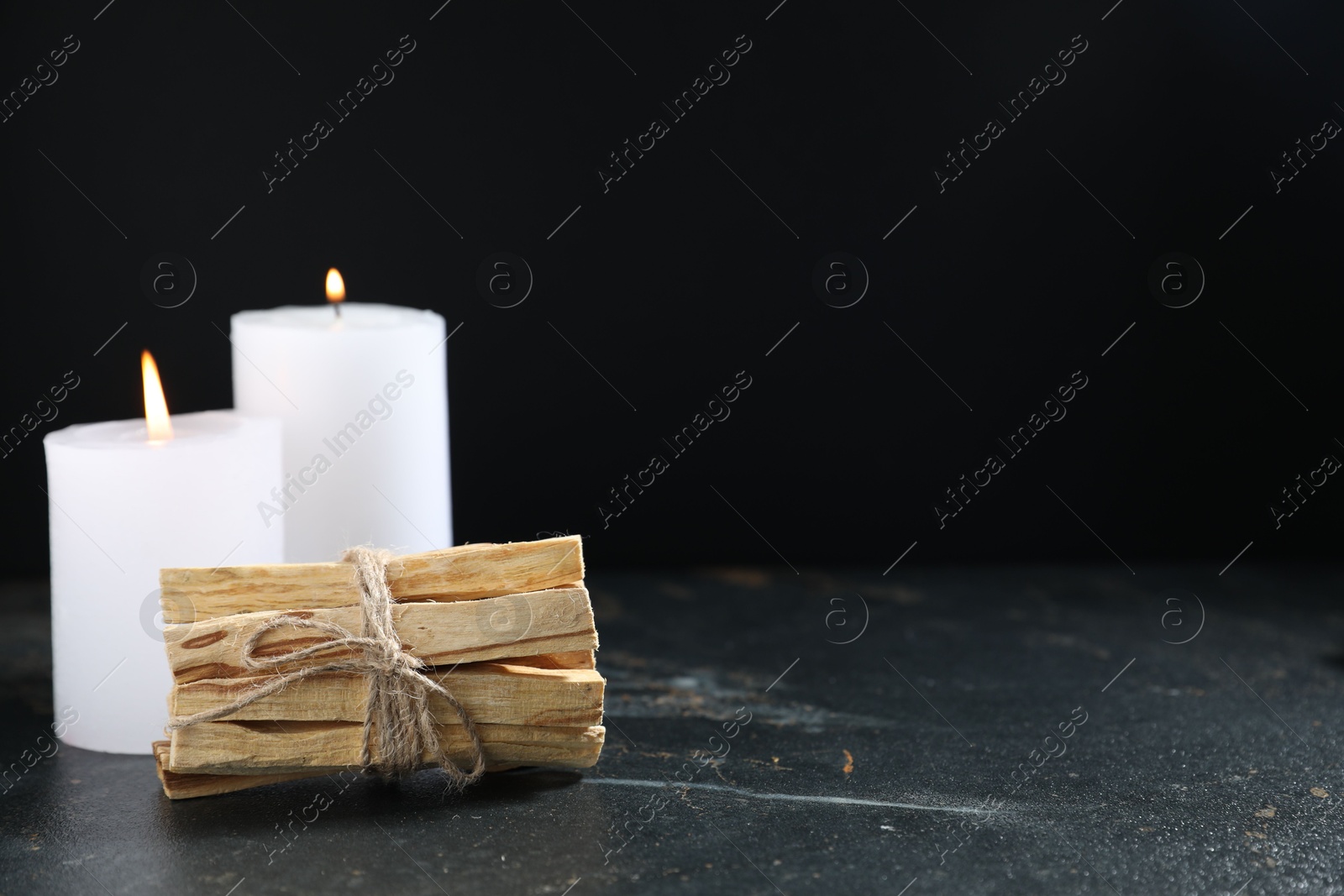 Photo of Bunch of palo santo sticks and burning candles on dark table, space for text