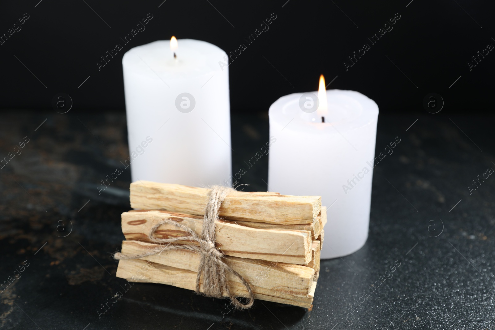 Photo of Bunch of palo santo sticks and burning candles on dark table, closeup